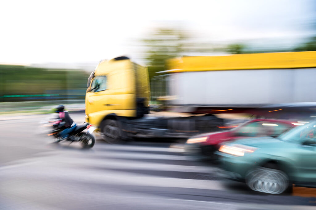 Depiction of dangerous city traffic. A motorcyclist and a truck are in motion blur to indicate movement at an intersection.